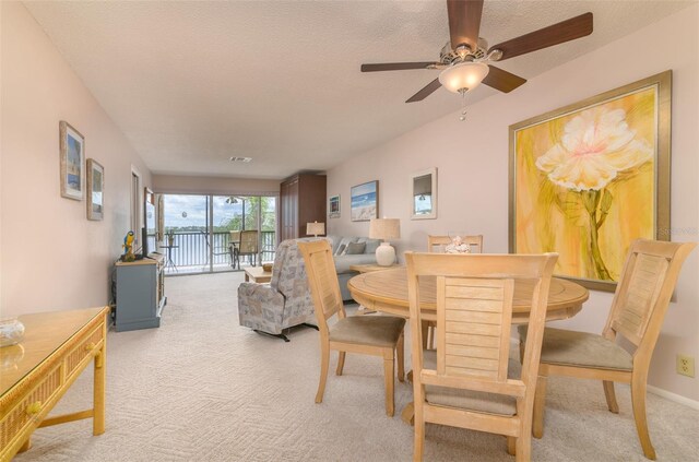 dining room featuring light carpet, ceiling fan, and a textured ceiling