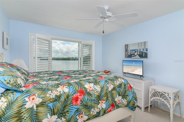 carpeted bedroom featuring a water view, access to outside, ceiling fan, and a textured ceiling