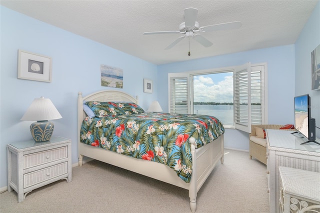 carpeted bedroom featuring a water view, a textured ceiling, and ceiling fan