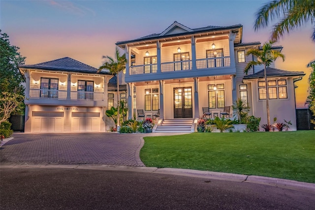 view of front of house featuring a yard, french doors, a balcony, covered porch, and a garage