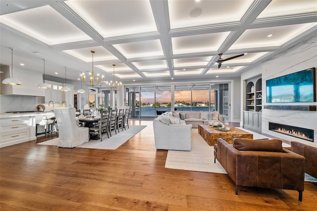 living room with a high end fireplace, coffered ceiling, ceiling fan with notable chandelier, light hardwood / wood-style flooring, and beam ceiling