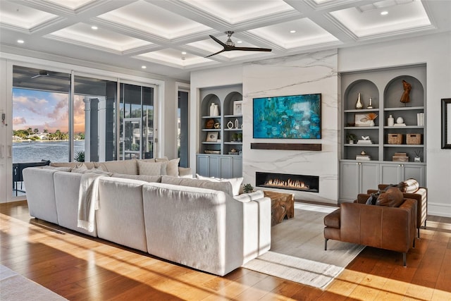 living room featuring coffered ceiling, built in shelves, beam ceiling, a fireplace, and light hardwood / wood-style floors