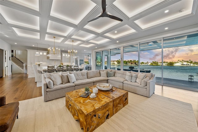 living room with coffered ceiling, ceiling fan with notable chandelier, a water view, light hardwood / wood-style flooring, and beamed ceiling