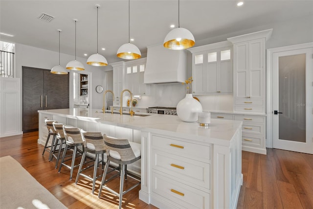 kitchen with a large island with sink, decorative light fixtures, white cabinetry, and premium range hood