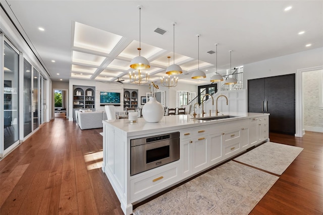 kitchen with a kitchen island with sink, sink, pendant lighting, dark hardwood / wood-style floors, and white cabinetry