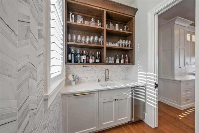 bar featuring wine cooler, decorative backsplash, light hardwood / wood-style flooring, and sink