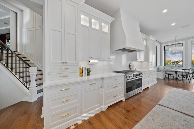 kitchen featuring hardwood / wood-style flooring, custom exhaust hood, white cabinetry, and high end stainless steel range oven