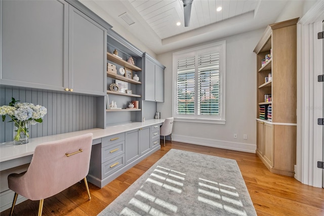 home office featuring light wood-type flooring, built in desk, and a tray ceiling