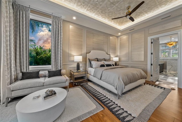 bedroom with connected bathroom, ceiling fan, crown molding, a tray ceiling, and hardwood / wood-style flooring