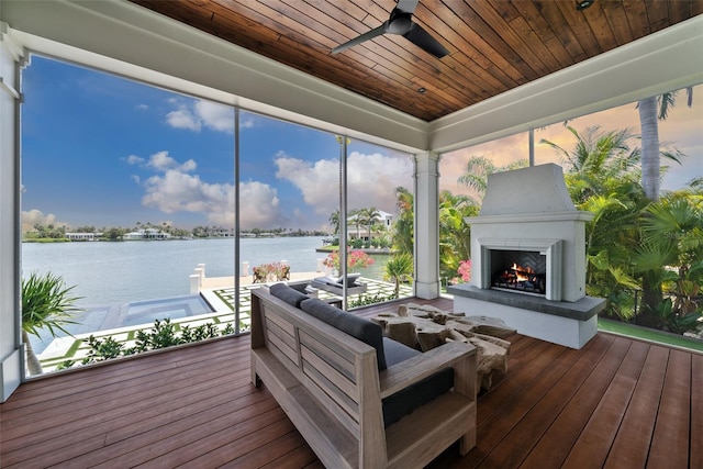 sunroom featuring ceiling fan, a water view, wood ceiling, and exterior fireplace