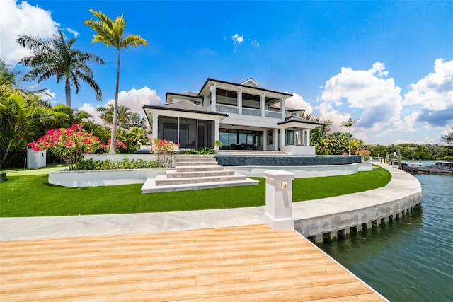 back of property with a sunroom, a water view, and a yard