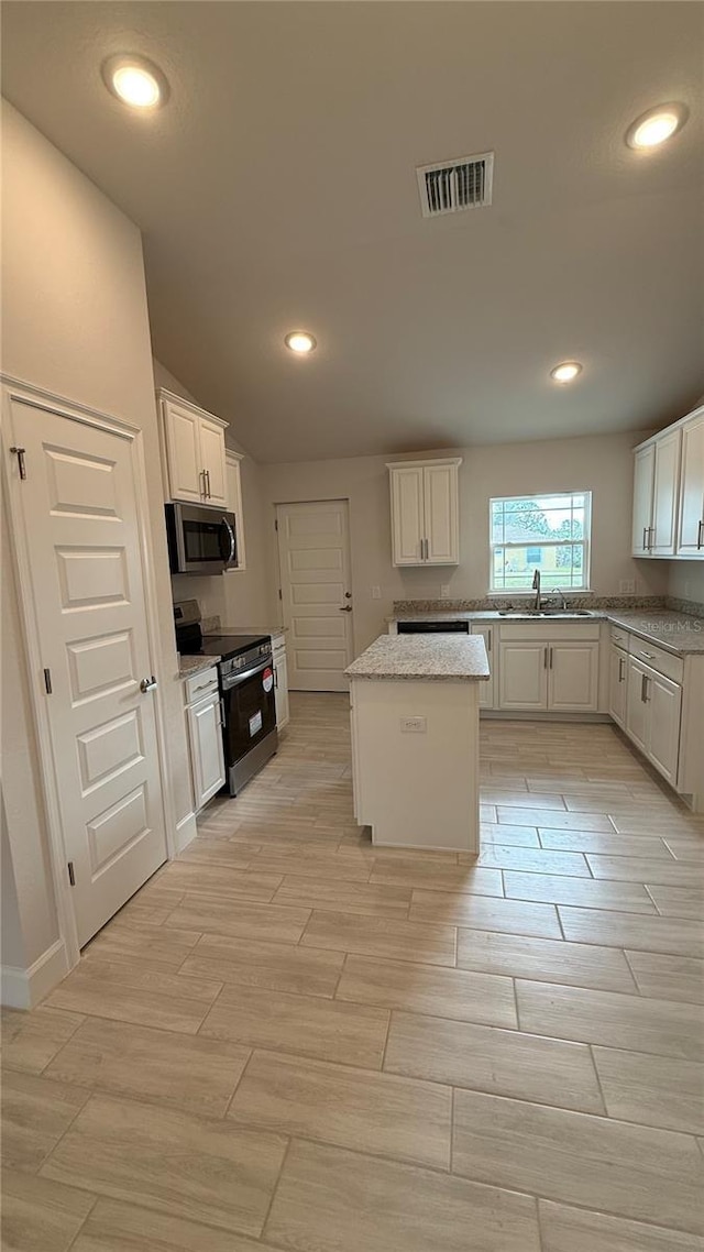 kitchen with black electric range oven, lofted ceiling, light stone countertops, a kitchen island, and white cabinetry