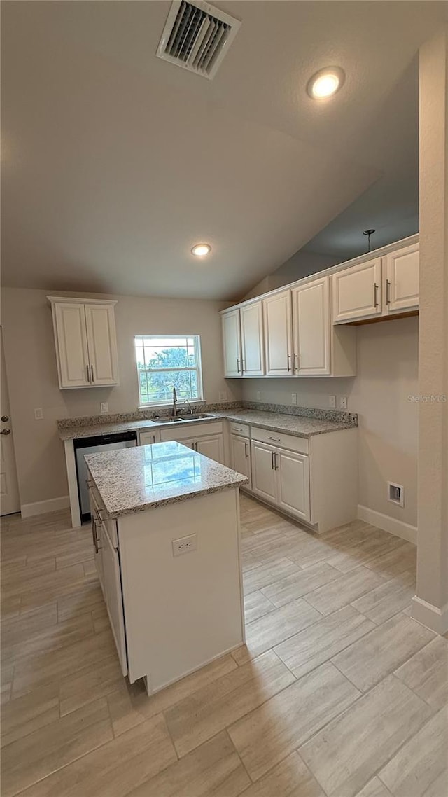 kitchen featuring lofted ceiling, light hardwood / wood-style flooring, stainless steel dishwasher, a kitchen island, and white cabinetry