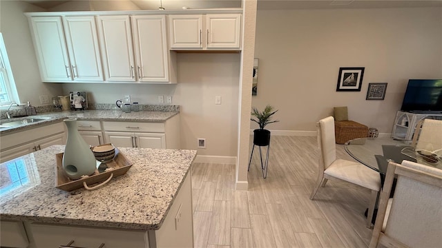 kitchen with light stone counters, light wood-type flooring, a sink, and white cabinets