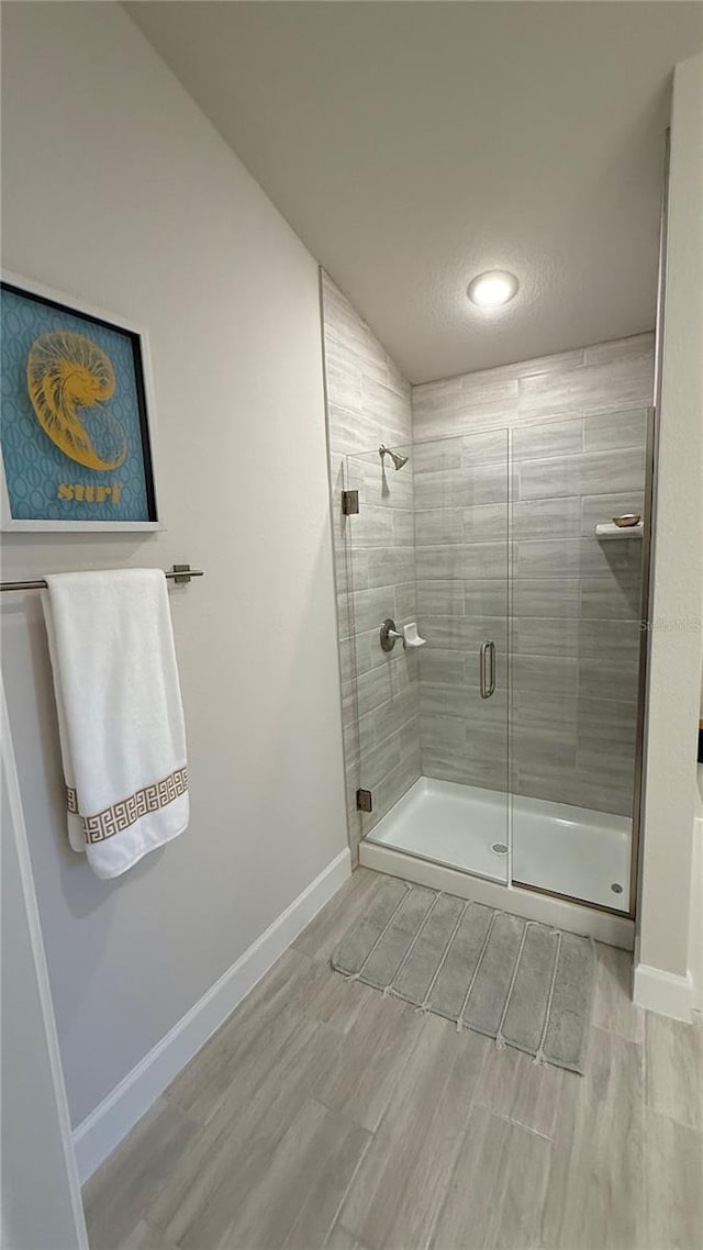 bathroom with lofted ceiling, a shower stall, baseboards, and wood finish floors