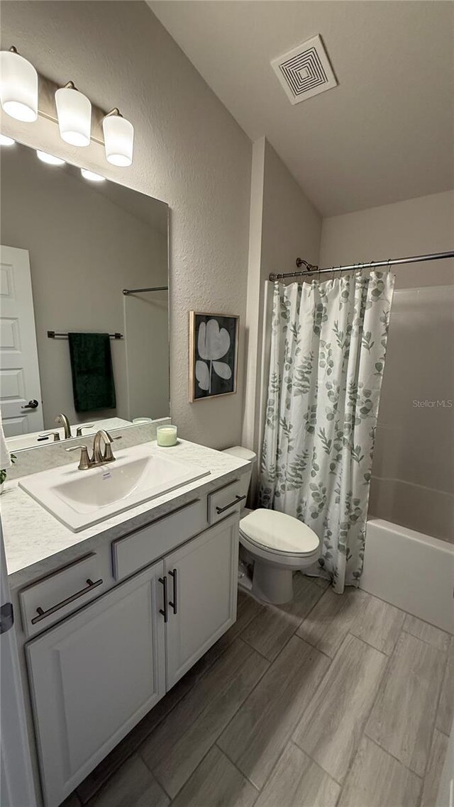 full bath with wood finish floors, visible vents, a textured wall, shower / bathtub combination with curtain, and vanity