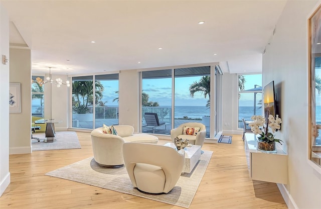 living room featuring a wall of windows, a chandelier, light hardwood / wood-style floors, and a water view