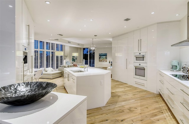 kitchen featuring black electric stovetop, a center island with sink, sink, hanging light fixtures, and white cabinets