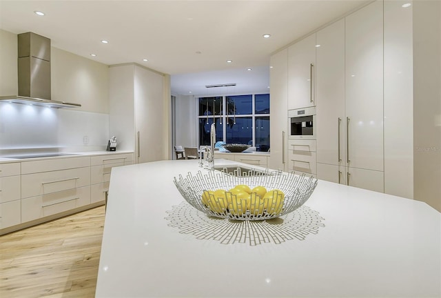 kitchen with white cabinetry, wall chimney range hood, black electric stovetop, light hardwood / wood-style floors, and oven