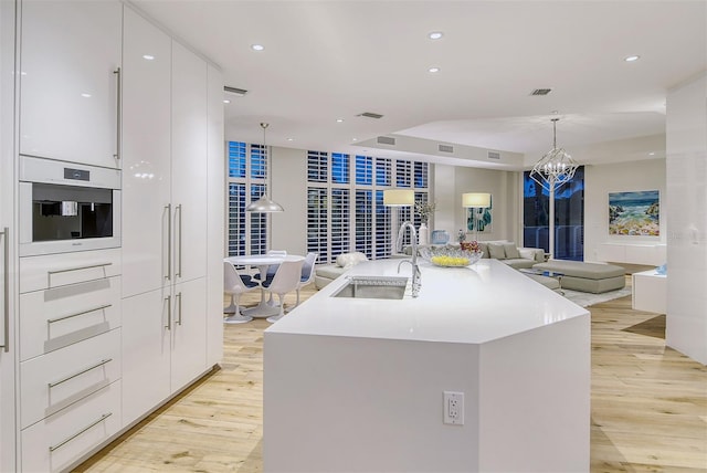 kitchen with white oven, an island with sink, pendant lighting, white cabinets, and sink