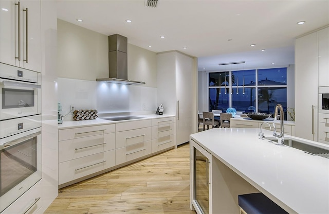 kitchen with wall chimney range hood, sink, white cabinetry, double oven, and black electric cooktop