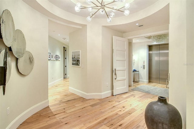 corridor with elevator, a chandelier, and light wood-type flooring