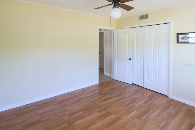 unfurnished bedroom featuring ceiling fan, a closet, crown molding, and hardwood / wood-style flooring