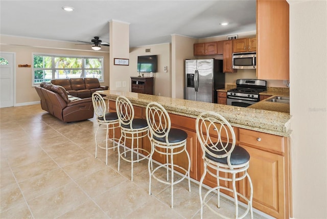 kitchen featuring light stone countertops, kitchen peninsula, appliances with stainless steel finishes, and a kitchen bar