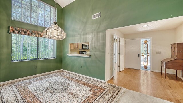 entryway with high vaulted ceiling, a notable chandelier, and light hardwood / wood-style flooring