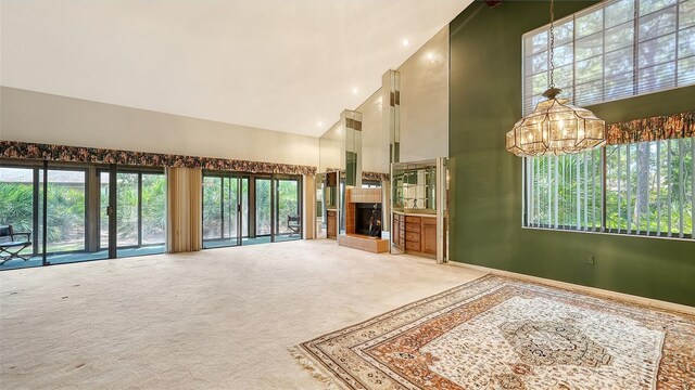 unfurnished living room with carpet floors, high vaulted ceiling, a notable chandelier, and a tile fireplace