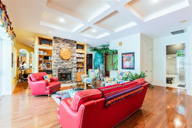 living room with coffered ceiling, beamed ceiling, light hardwood / wood-style floors, built in features, and a stone fireplace