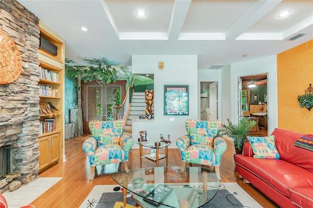 living room with beam ceiling, ceiling fan, a stone fireplace, and light wood-type flooring