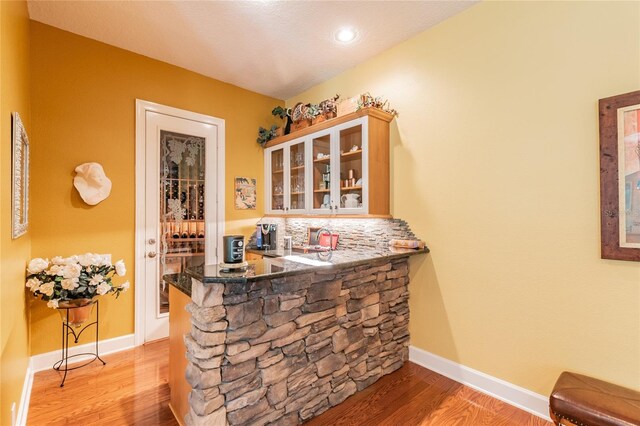 bar featuring dark stone counters, light hardwood / wood-style floors, and tasteful backsplash