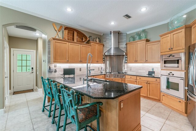 kitchen featuring tasteful backsplash, light tile floors, stainless steel appliances, wall chimney exhaust hood, and ornamental molding