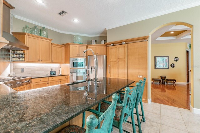 kitchen featuring light tile floors, crown molding, backsplash, stainless steel appliances, and wall chimney exhaust hood