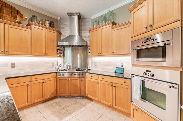 kitchen with dark stone counters, ornamental molding, stainless steel gas stovetop, wall chimney exhaust hood, and tasteful backsplash