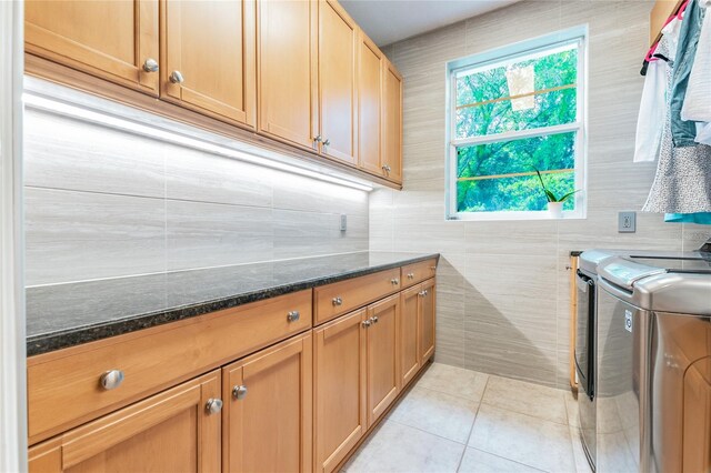 laundry room featuring washing machine and dryer, cabinets, light tile flooring, and tile walls