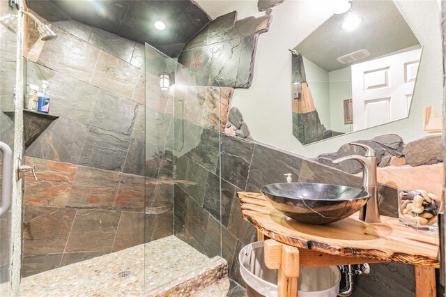 bathroom with tile walls, sink, and tiled shower