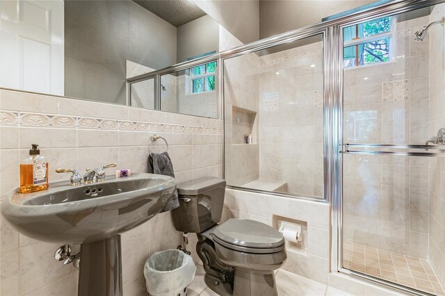 bathroom featuring backsplash, tile walls, tile floors, toilet, and a shower with shower door