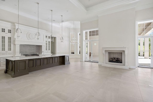 interior space featuring decorative light fixtures, a center island with sink, a towering ceiling, and light tile floors