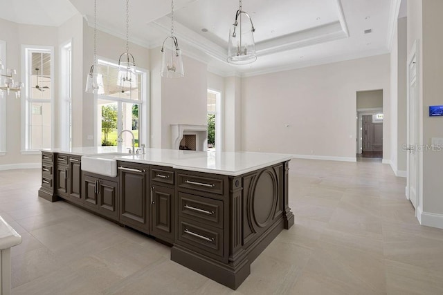 kitchen with sink, light tile flooring, a raised ceiling, and a kitchen island with sink