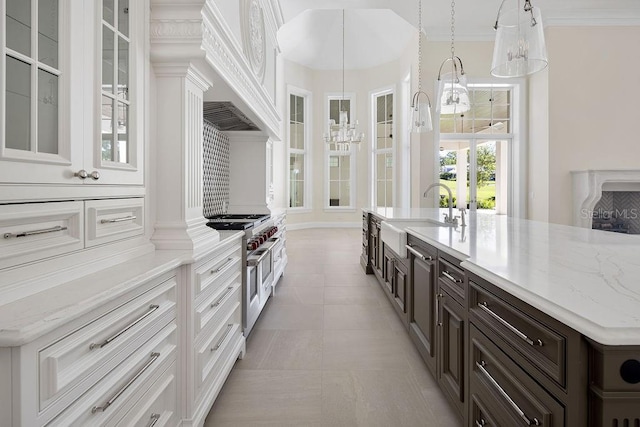 kitchen with sink, white cabinetry, decorative light fixtures, range with two ovens, and light stone countertops