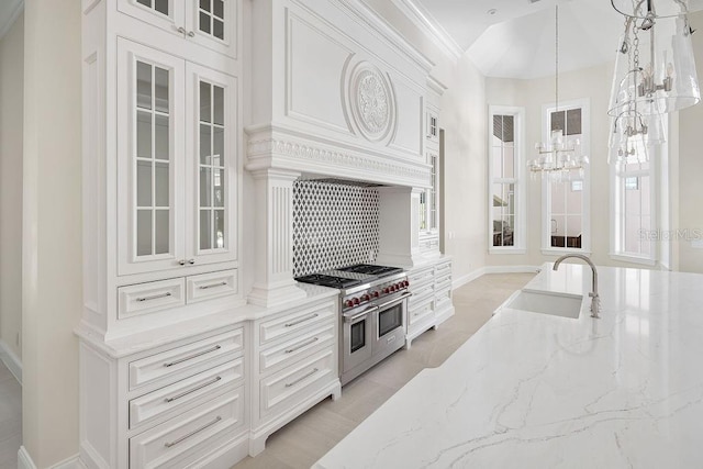 kitchen featuring sink, backsplash, white cabinetry, decorative light fixtures, and range with two ovens