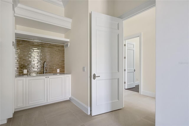 bar featuring light stone counters, light tile floors, white cabinets, sink, and crown molding