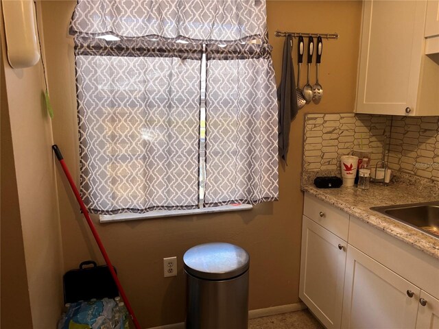 kitchen with white cabinetry, backsplash, sink, and light stone countertops