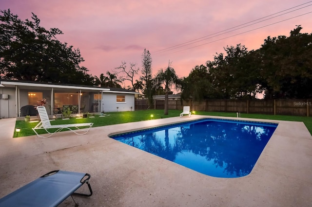 pool at dusk featuring a patio area and a lawn