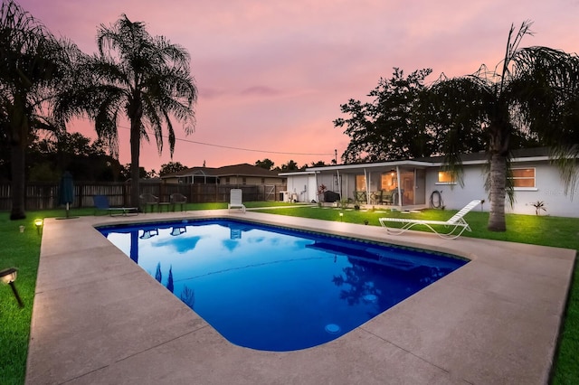 pool at dusk featuring a lawn