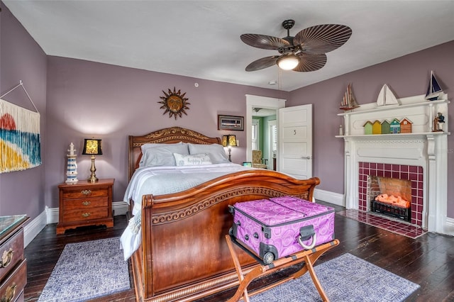 bedroom with ceiling fan, dark wood-type flooring, and a tile fireplace