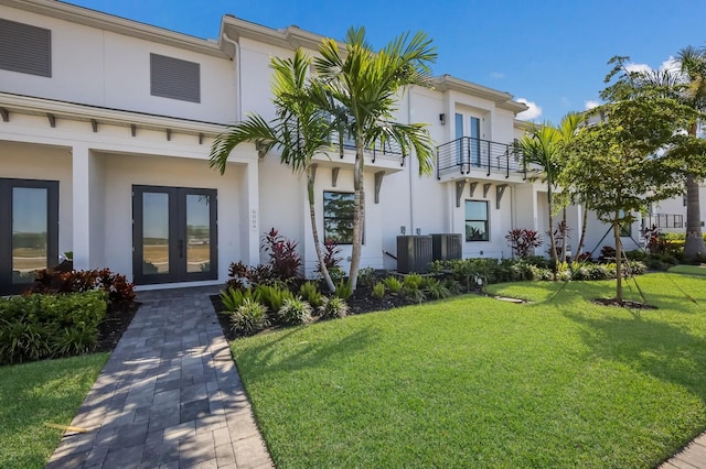 exterior space featuring a front lawn, a balcony, stucco siding, and french doors