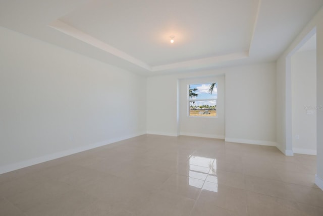 spare room with baseboards, light tile patterned floors, and a raised ceiling
